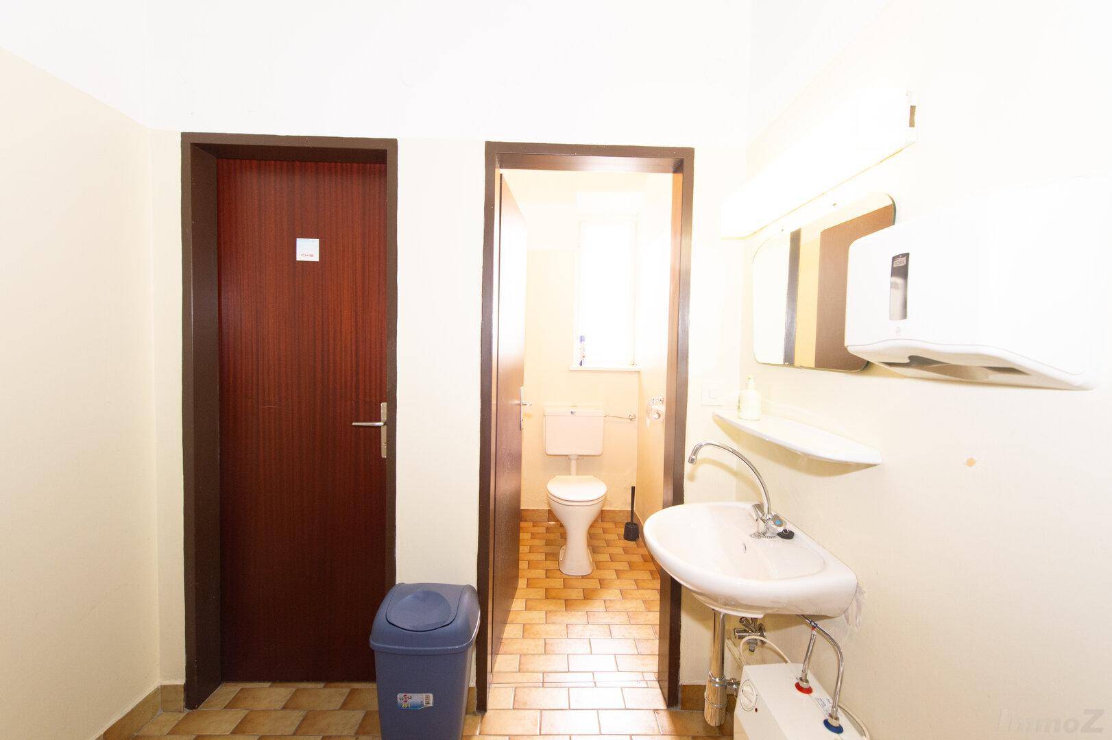Einfache Gästetoilette mit Waschbecken und Fenster, funktional und sauber.