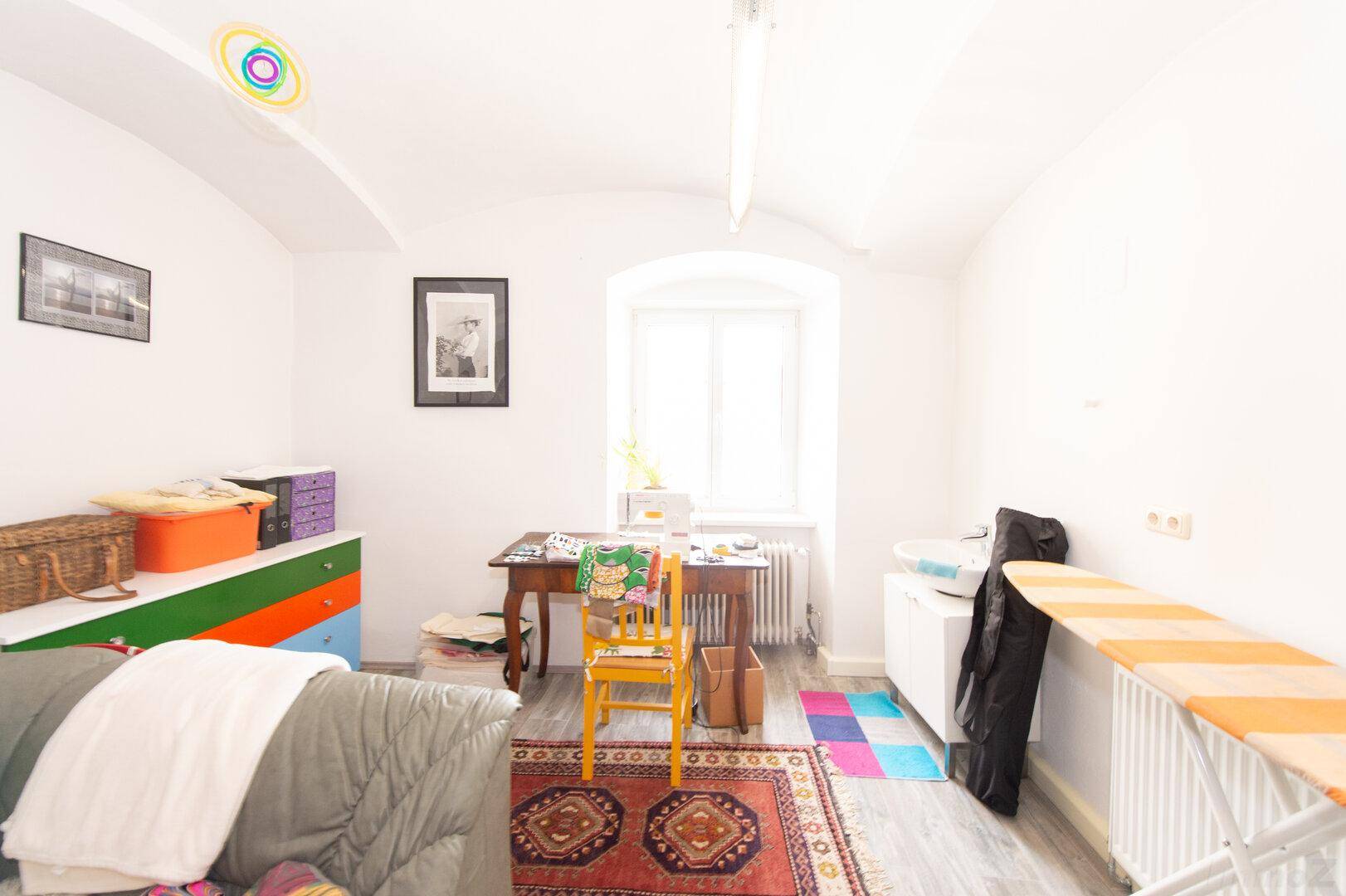 Heller Raum mit gewölbter Decke, Fenster und einem bunten Schrank, genutzt als Arbeits- oder Hobbybereich.