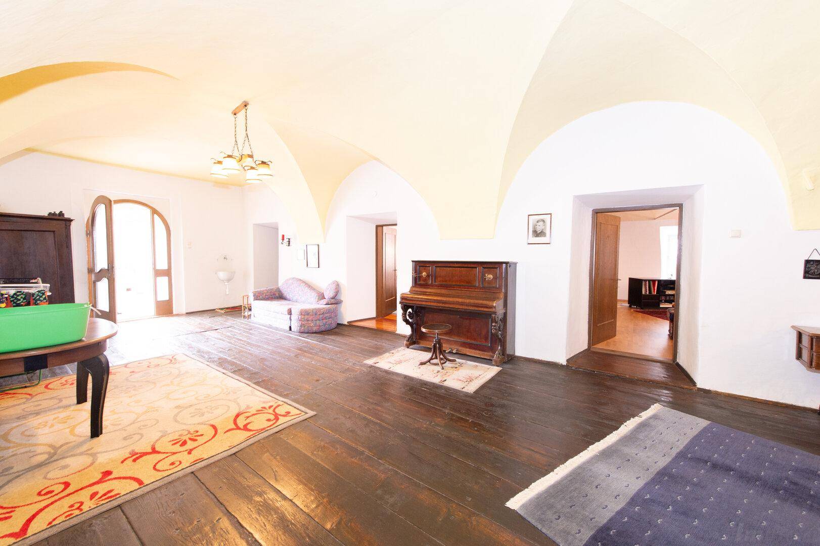 Geräumiger Wohnbereich mit dunklem Holzboden, gewölbter Decke und antiken Möbeln, sehr charaktervoll.