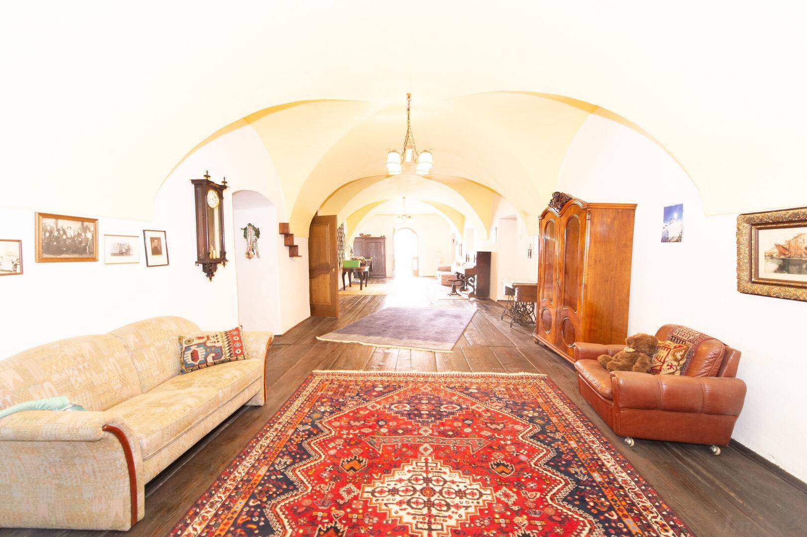 Langer Wohnbereich mit dunklem Holzboden, gewölbter Decke und antiken Möbeln, sehr weitläufig.