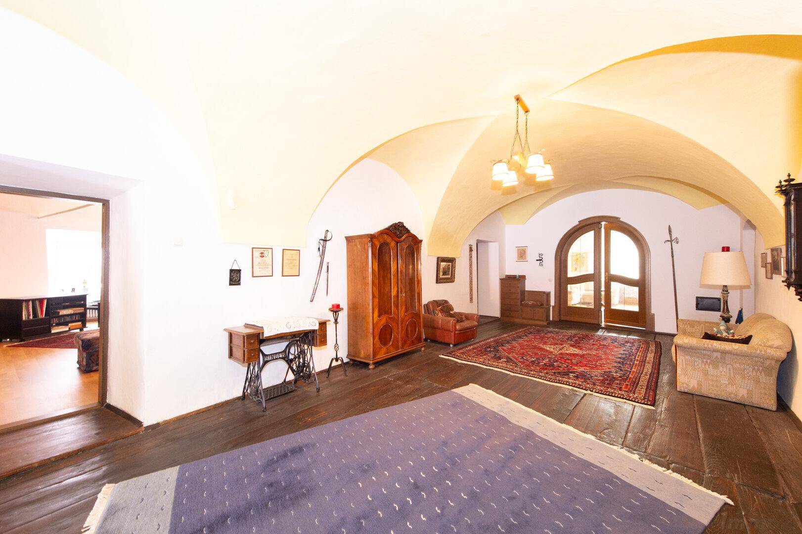 Großer Wohnraum mit dunklem Holzboden, gewölbter Decke und antiken Möbeln, sehr einladend.