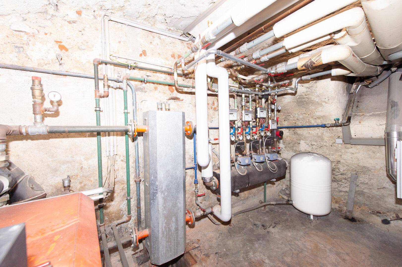 Heizungsraum im Keller mit zahlreichen Rohren, Heizkessel und technischen Installationen.