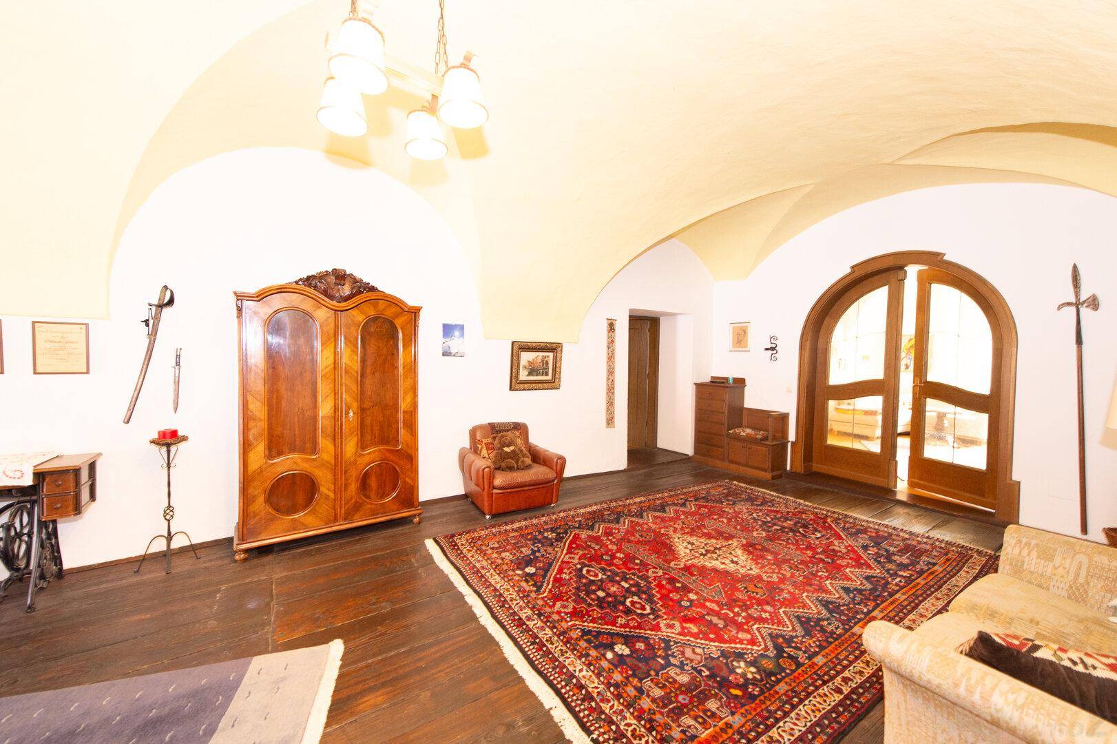 Geräumiger Wohnbereich mit dunklem Holzboden, gewölbter Decke und antiken Möbeln, sehr elegant.