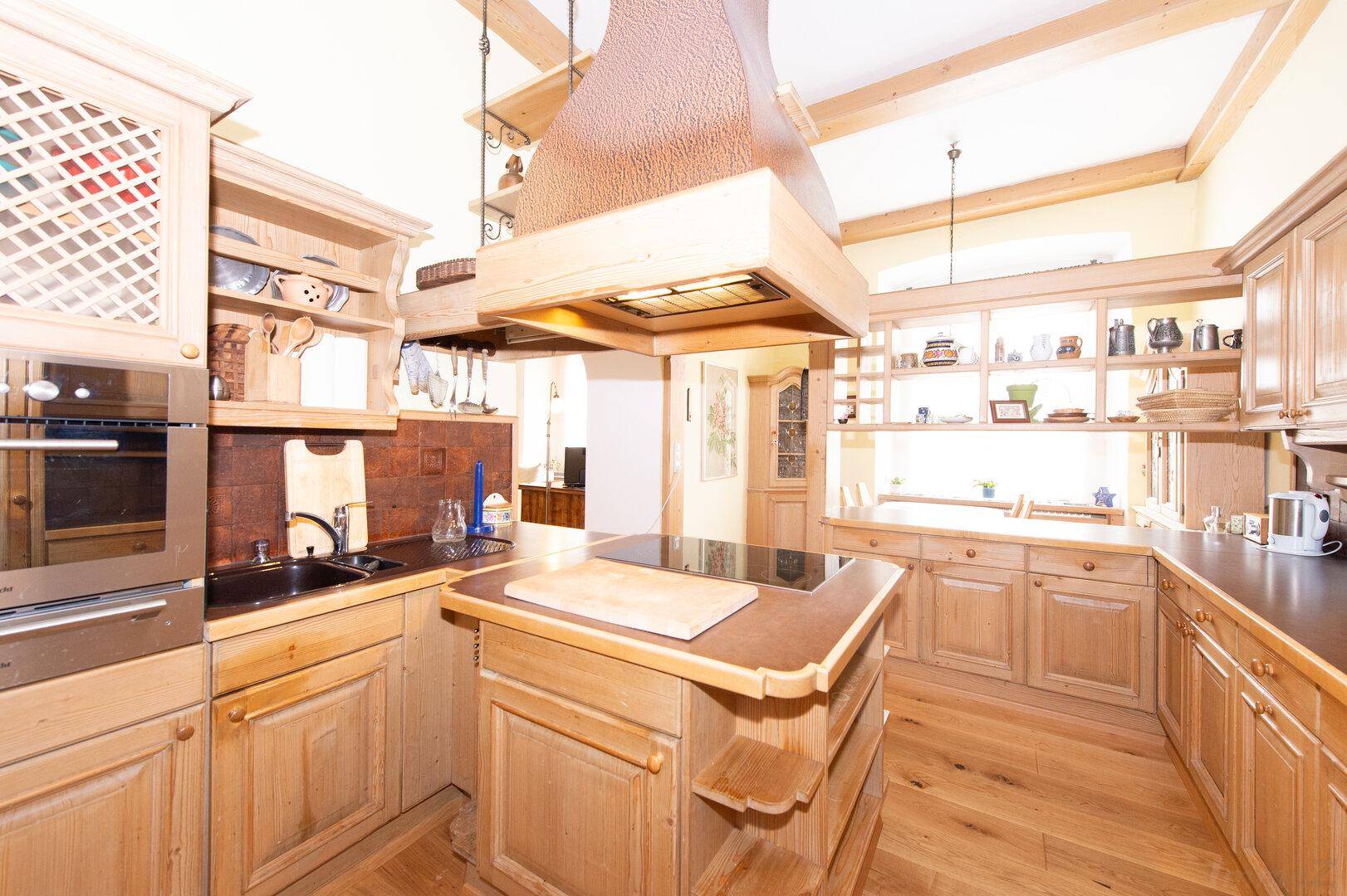 Traditionelle Holzküche mit Kochinsel, Einbaugeräten und Holzbalken an der Decke.