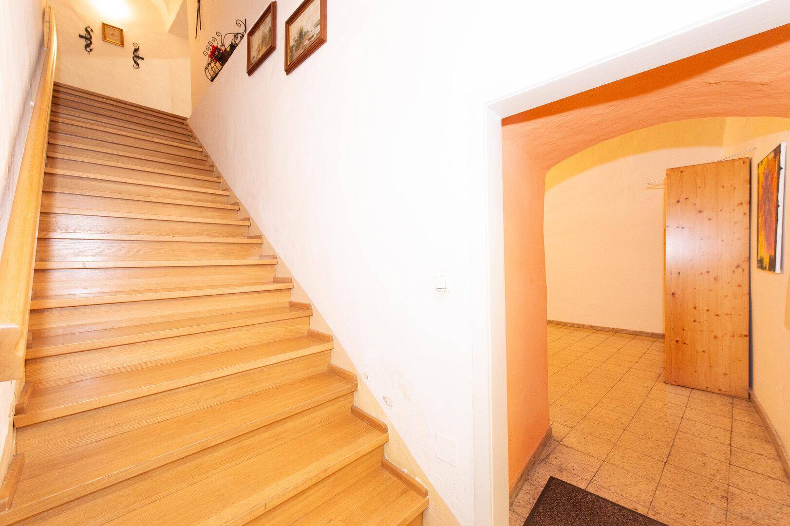 Holztreppe führt zu einem Flur mit gefliestem Boden und gewölbter Decke, typisch für Altbau.