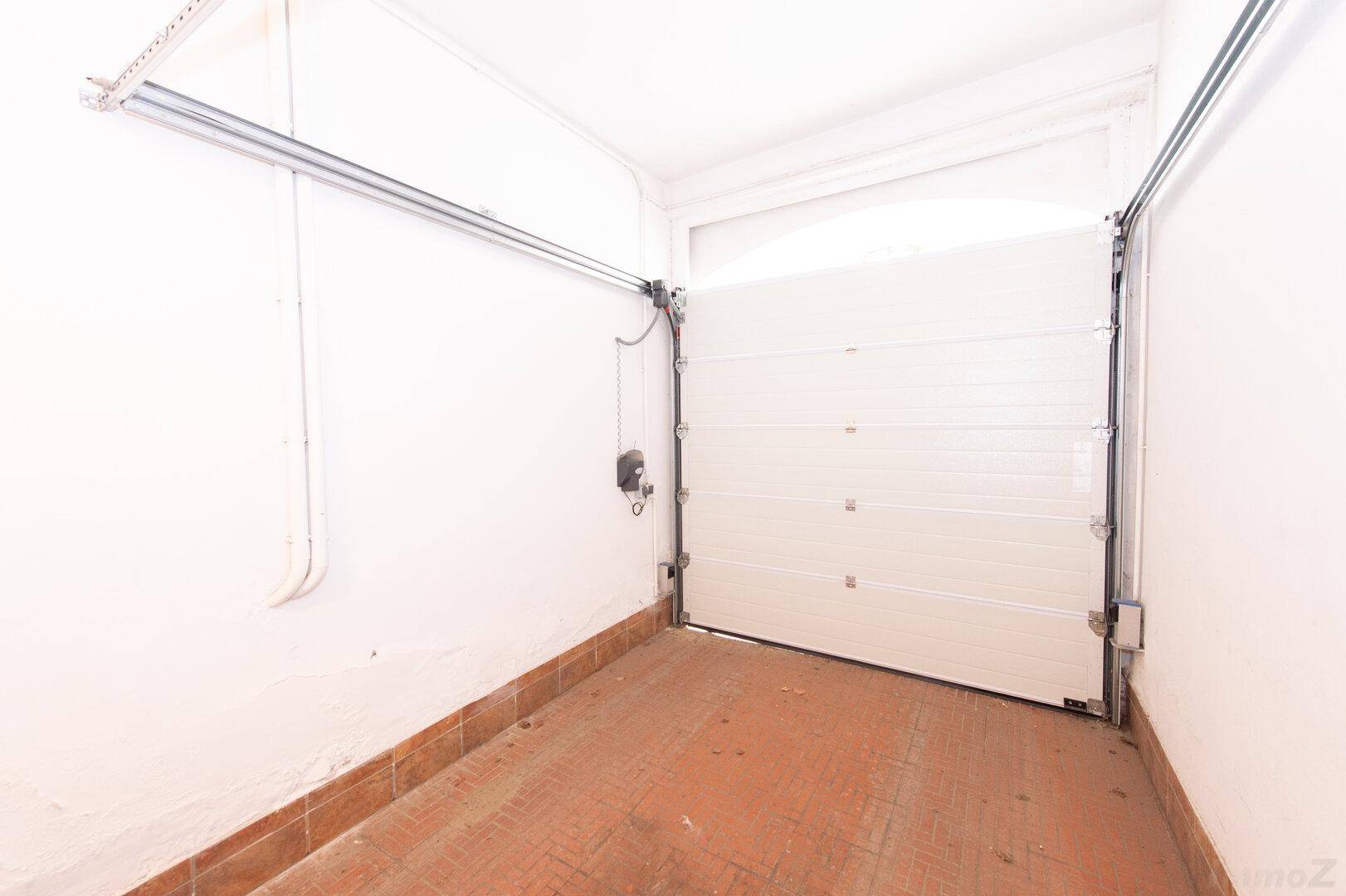 Innenansicht einer Garage mit einem weißen Sektionaltor und Fliesenboden.