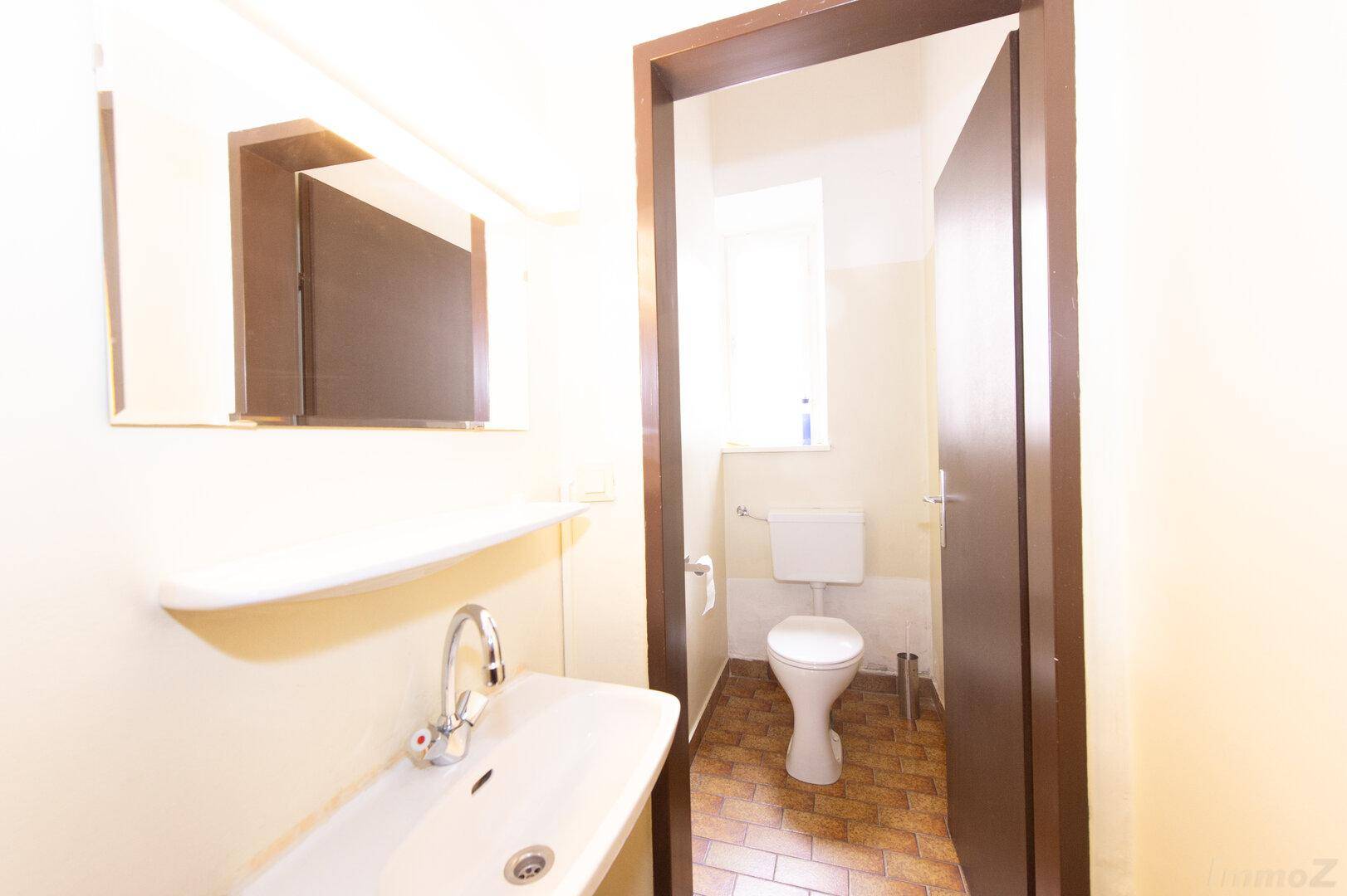 Helle Gästetoilette mit Waschbecken, Spiegel und Fenster, in gutem Zustand.