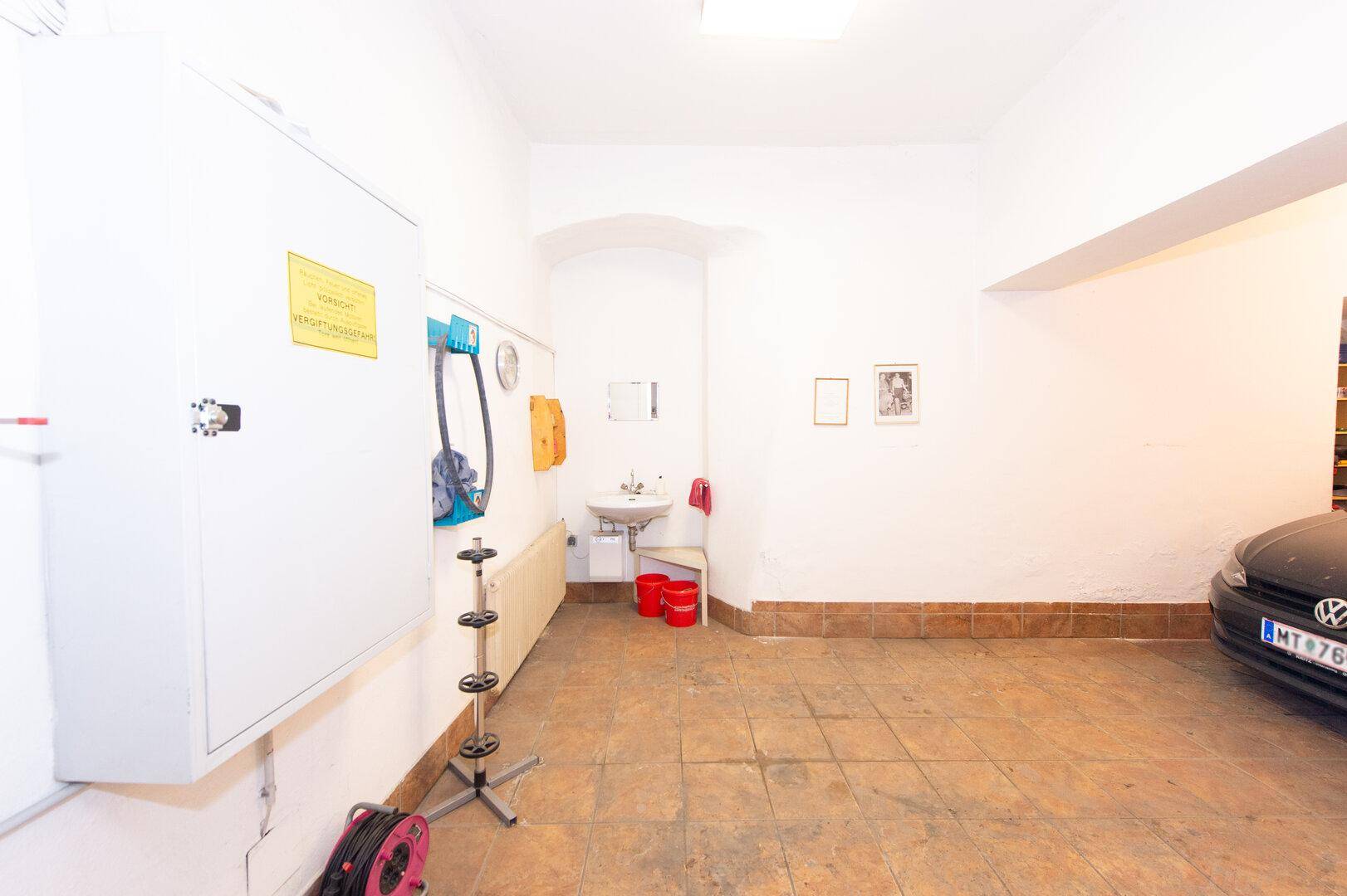Geräumige Garage mit Fliesenboden, Waschbecken und Stauraum, ideal für Fahrzeuge und Werkzeuge.