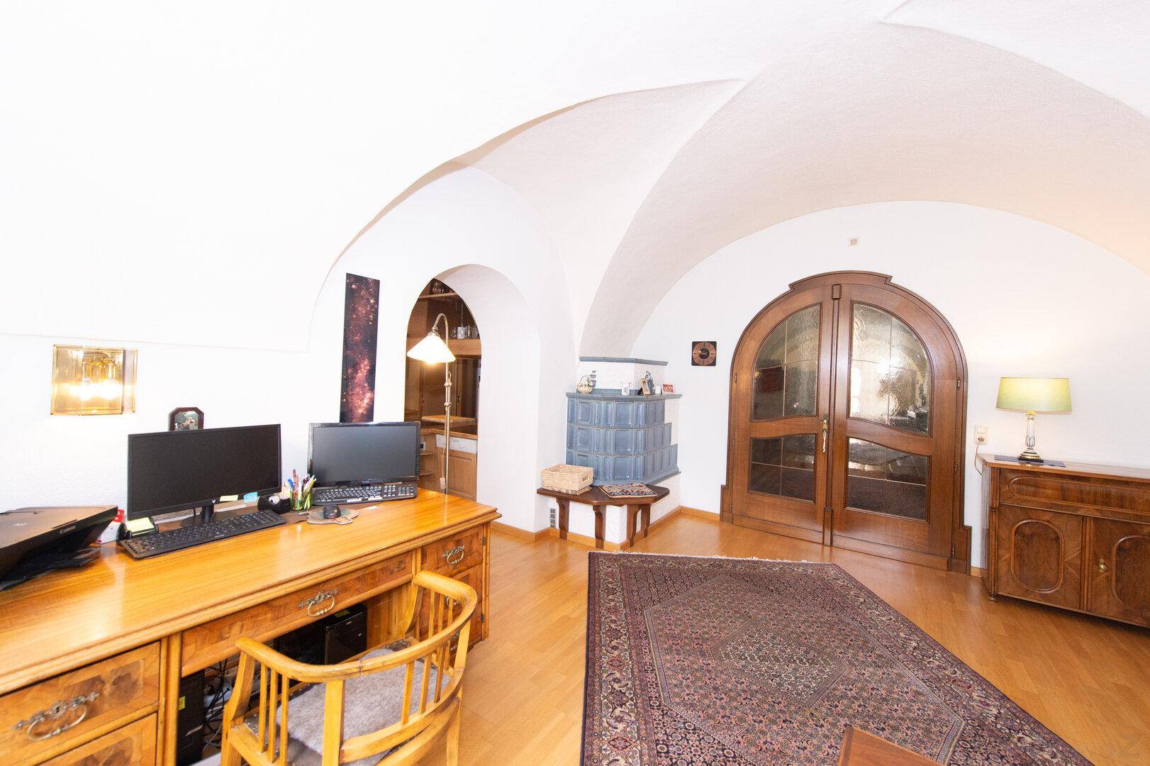 Detailansicht des Arbeitsbereichs mit gewölbter Decke, Holzboden und einem traditionellen Kachelofen.