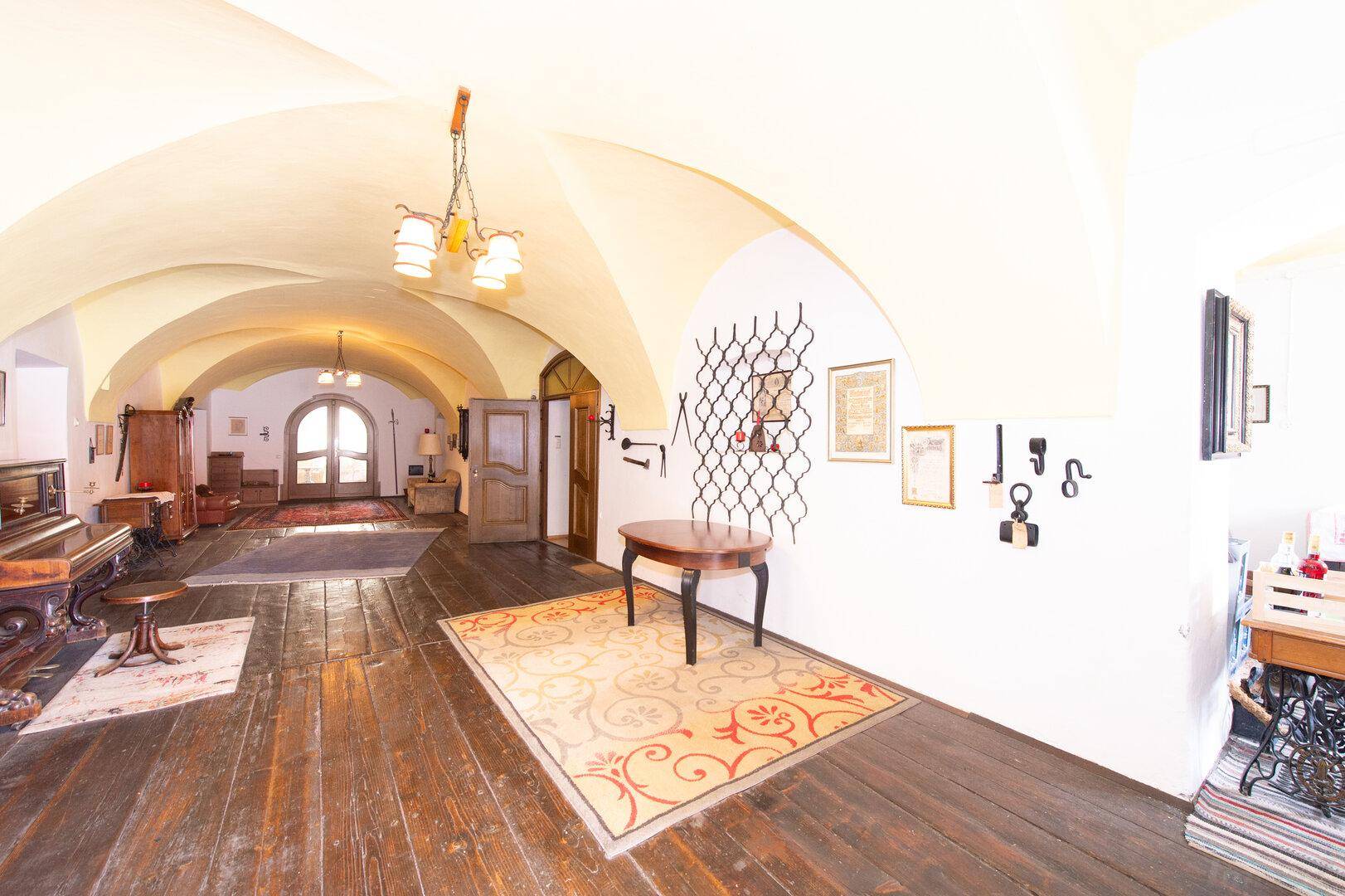 Langer Flur mit dunklem Holzboden, gewölbter Decke, einem Klavier und Holztüren am Ende.