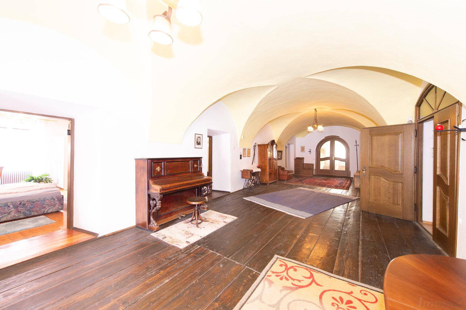 Geräumiger Flur mit dunklem Holzboden, gewölbter Decke und einem antiken Klavier.