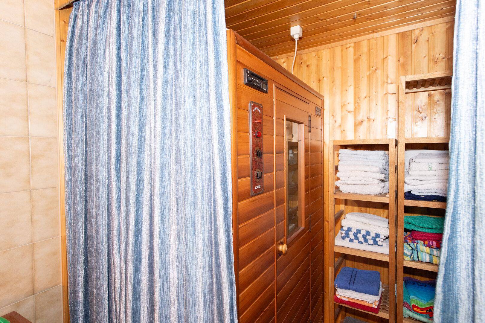 Nahaufnahme einer Holzsaunakabine im Badezimmerbereich, umgeben von Regalen und Handtüchern.