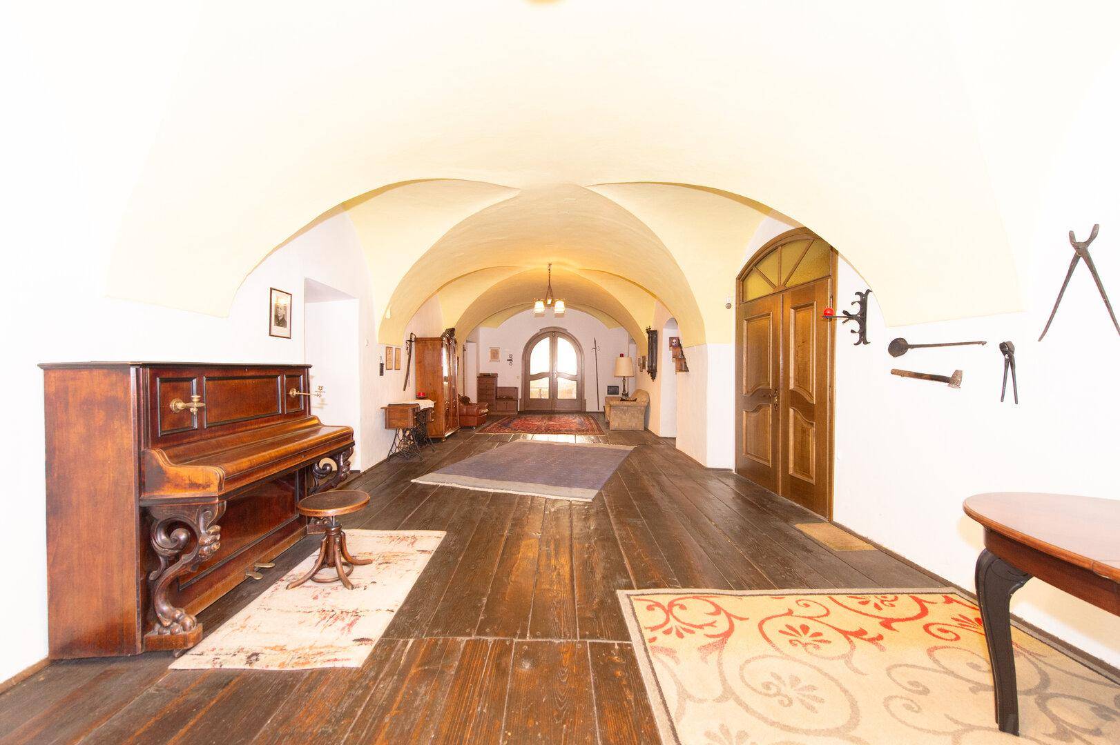 Langer Flur mit dunklem Holzboden, gewölbter Decke und einem antiken Klavier.