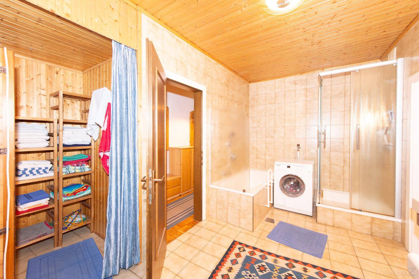 Badezimmer mit Waschmaschine, Duschkabine, Badewanne und einem praktischen Stauraum mit Regalen.
