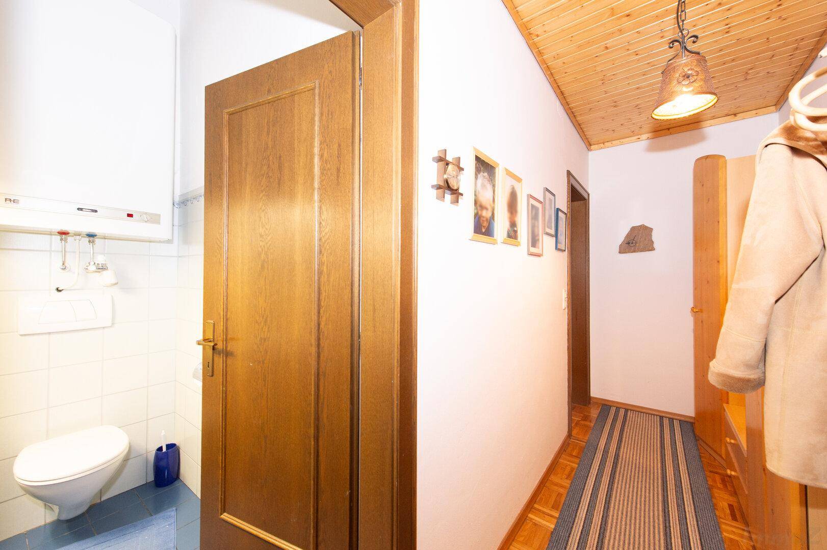 Flur mit Holztür, Garderobe und Blick auf eine kleine Toilette mit blauen Fliesen.