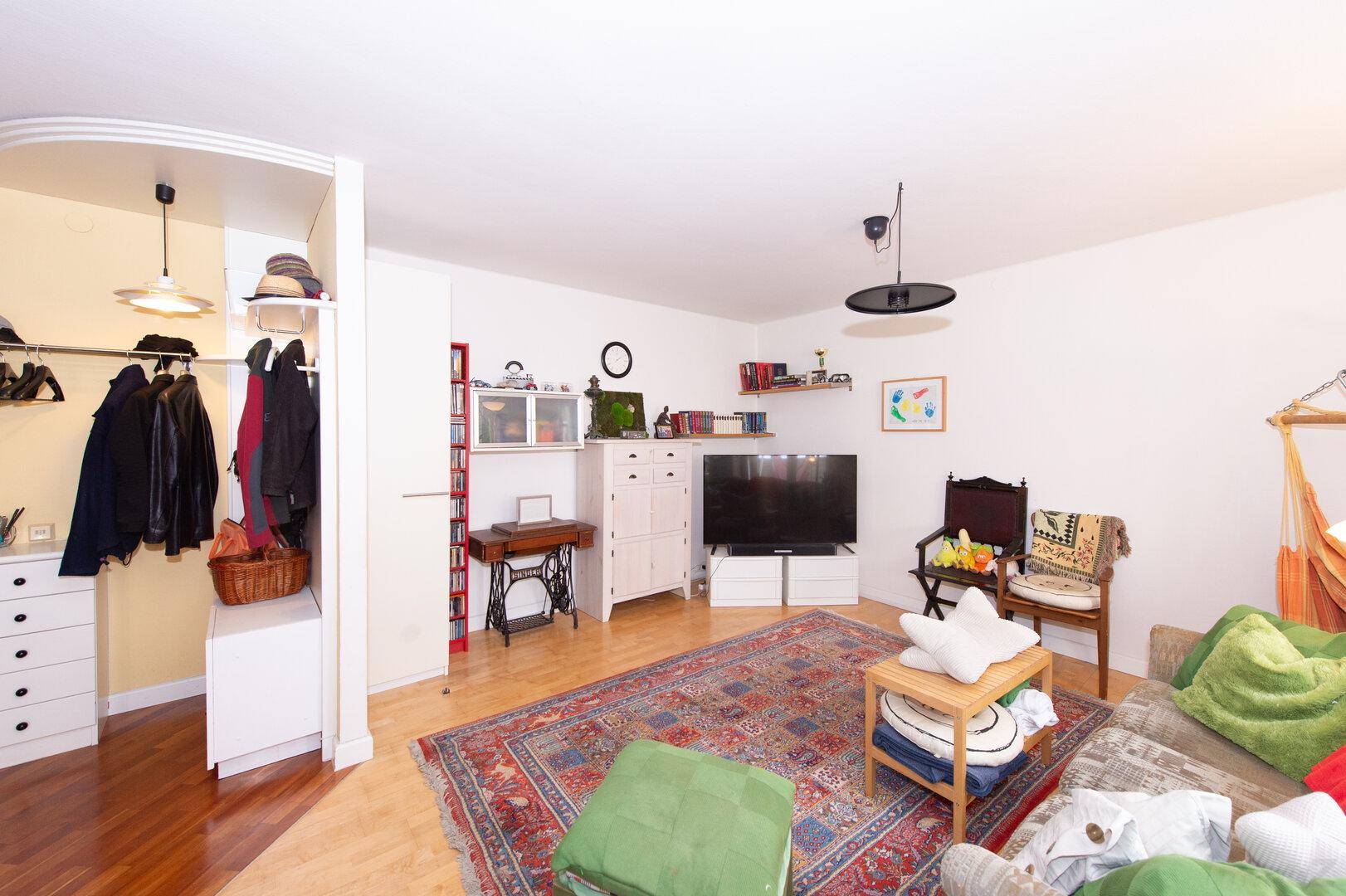 Wohnzimmer mit Fernseher, weißem Schrank und Blick auf den Flur mit Einbauschränken.