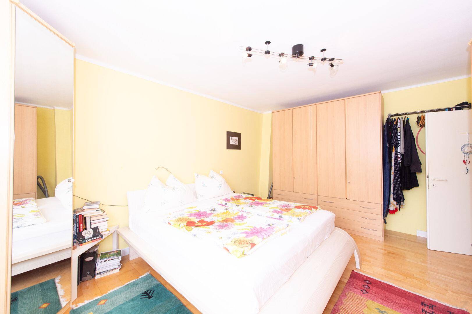Schlafzimmer mit Holzboden, gelben Wänden und großen Holzschränken, viel Stauraum.