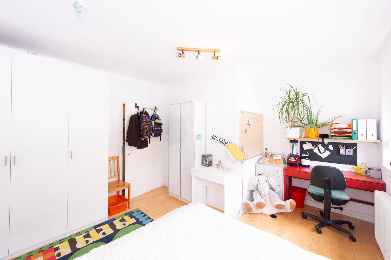 Kinderzimmer mit weißen Kleiderschränken, Schreibtisch und Holzboden, hell und funktional.