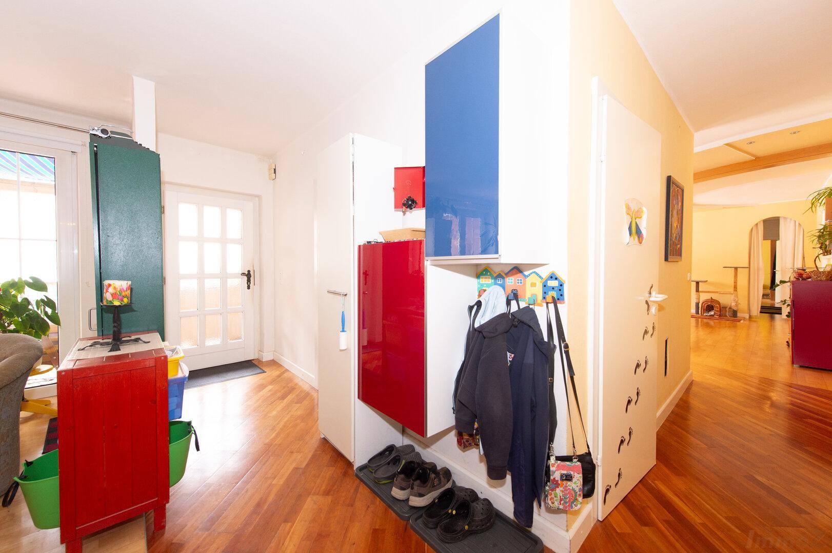 Eingangsbereich mit Holzboden, Garderobe und einer hellen Eingangstür, die viel Licht hereinlässt.