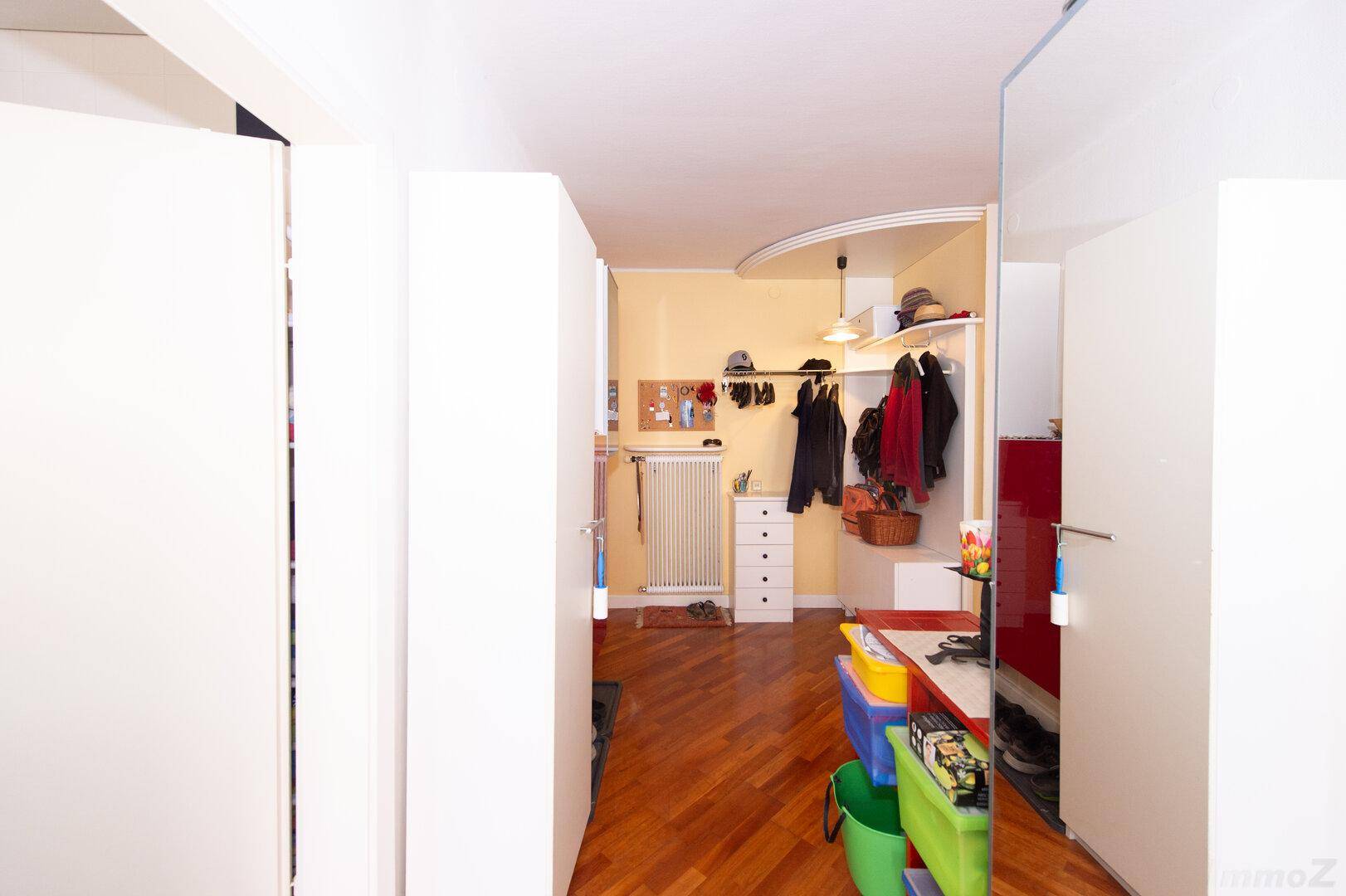Flur mit weißen Einbauschränken, einer Garderobe und einem hellen Holzparkettboden.
