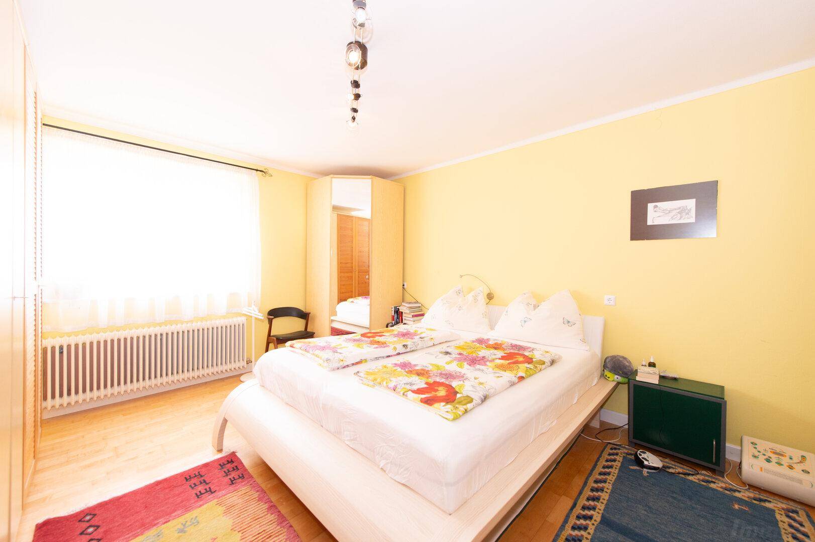 Geräumiges Schlafzimmer mit Doppelbett, gelben Wänden und Holzboden, sehr einladend.