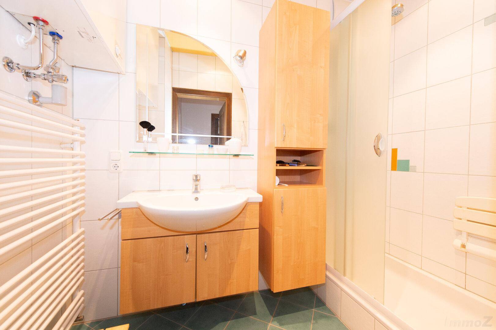 Modernes Badezimmer mit Waschtisch, Spiegel, Duschkabine und einem Handtuchheizkörper.