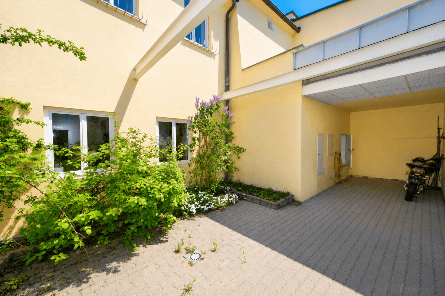 Heller Innenhof mit gepflastertem Bereich, grünen Pflanzen und Zugang zu einer überdachten Fläche.