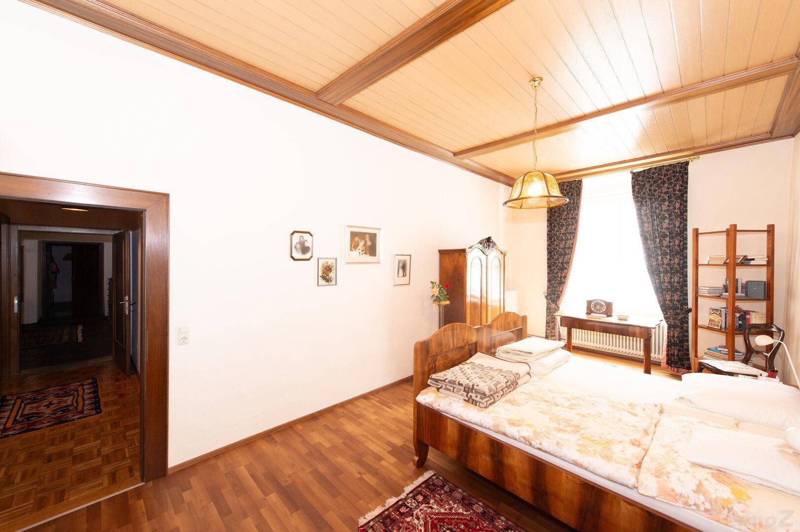 Schlafzimmer mit Holzbett, Kleiderschrank und einer Tür, die zu einem anderen Raum führt.