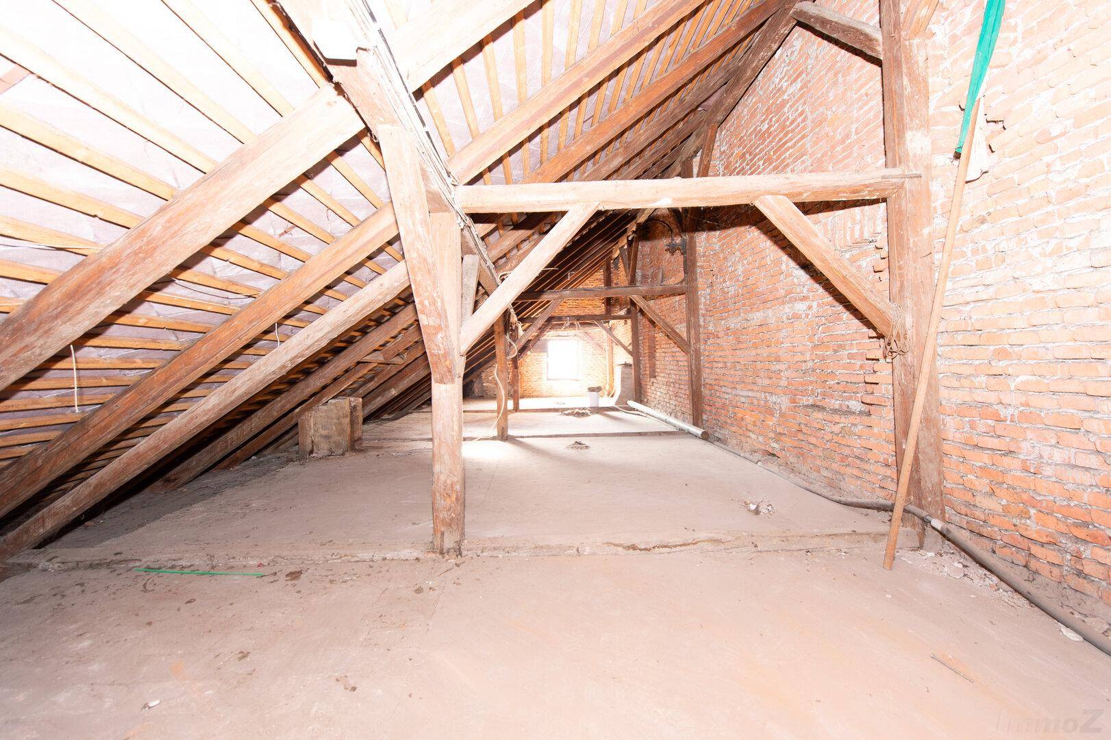 Unfertiger Dachboden mit sichtbaren Holzbalken und Ziegelwänden, bereit zum Ausbau.