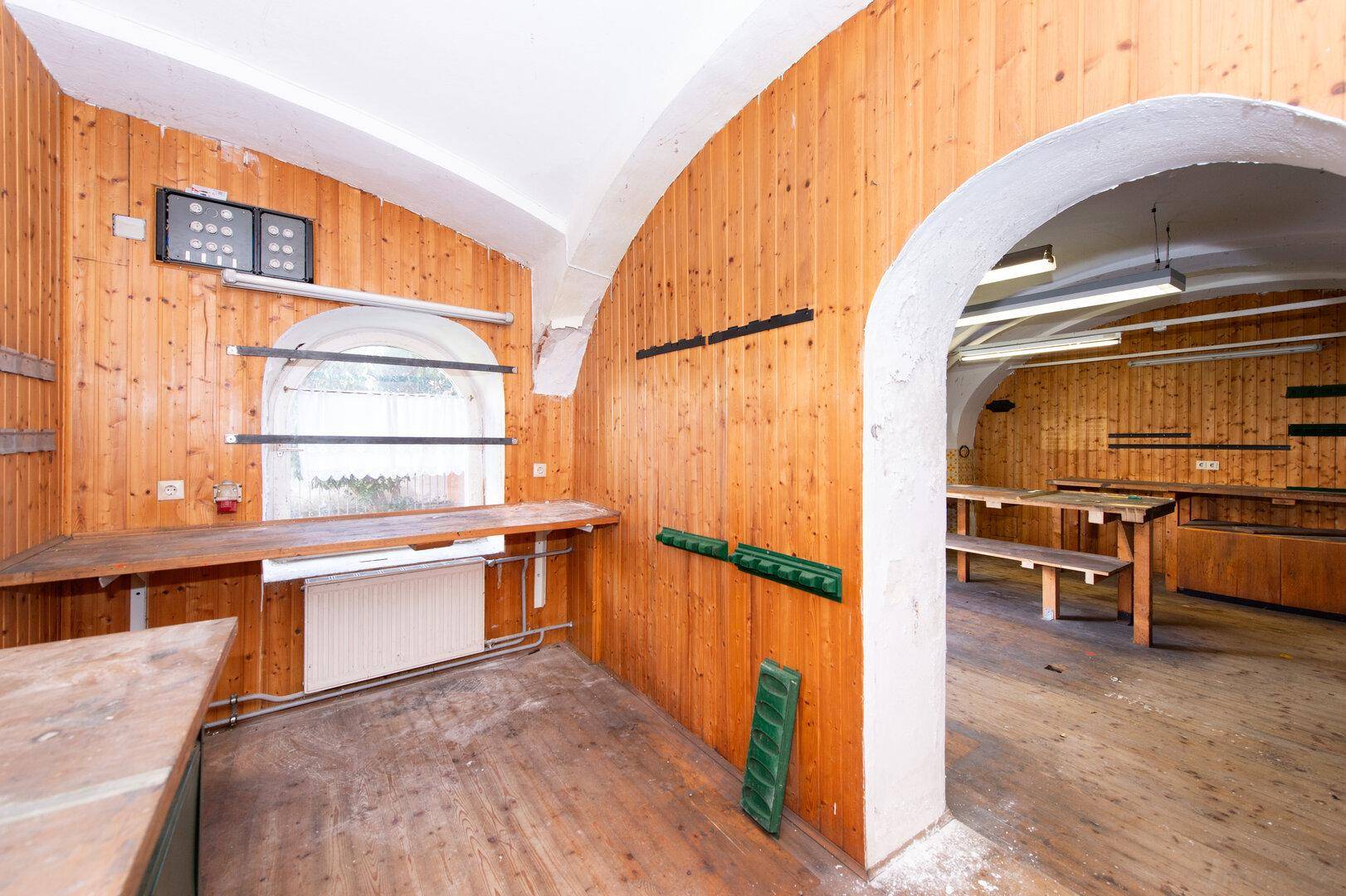 Großer Raum mit Holzvertäfelung, Werkbänken und einem Rundbogenfenster.