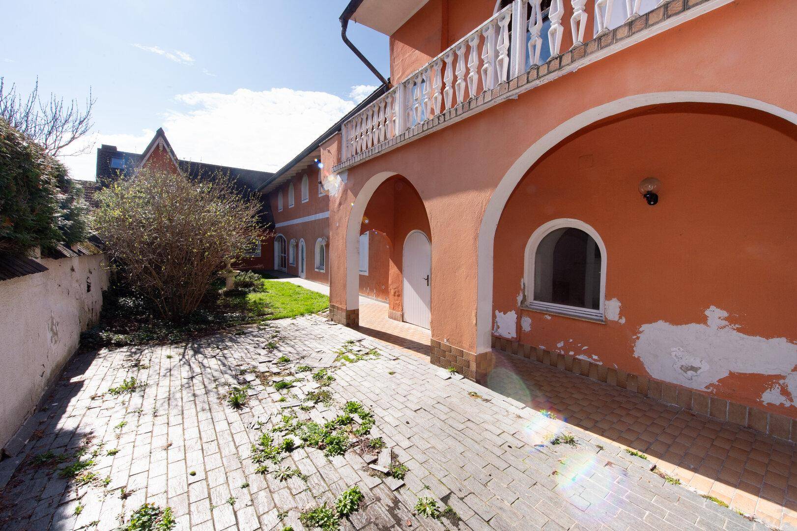Außenansicht eines Gebäudes mit orangefarbener Fassade, Bögen und einem Balkon mit Balustrade.