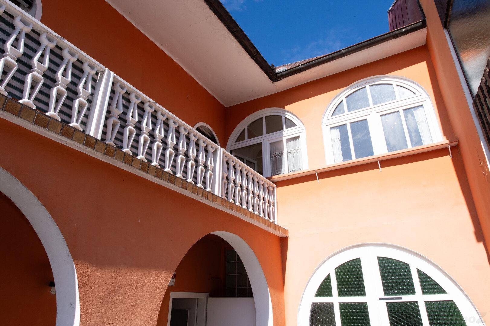 Detailansicht der orangefarbenen Fassade mit dekorativen Bögen und Rundbogenfenstern.