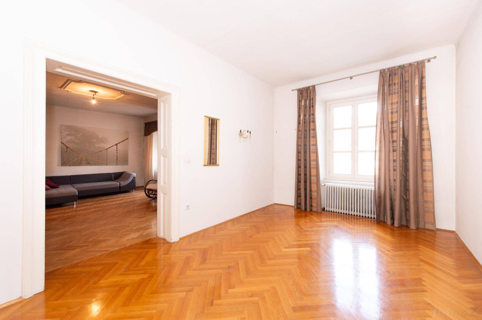 Geräumiges Wohnzimmer mit Fischgrätparkett und Blick in einen weiteren Wohnbereich.