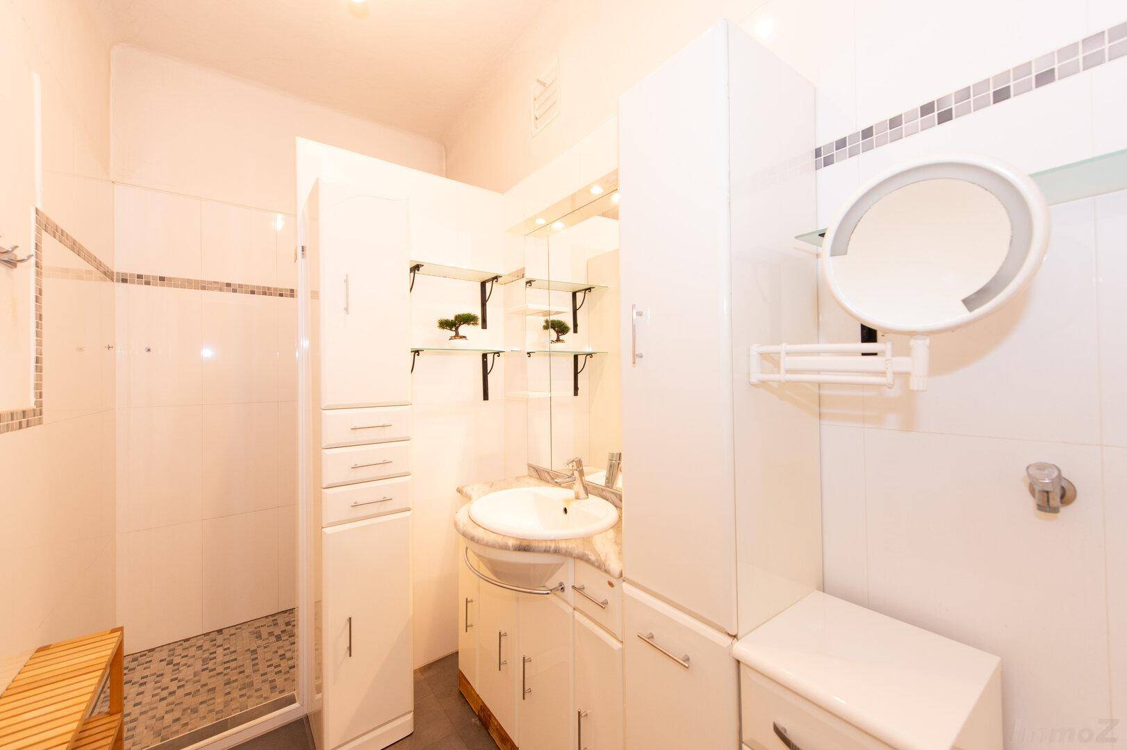 Modernes Badezimmer mit weißer Einrichtung, Dusche und integriertem Waschbecken.