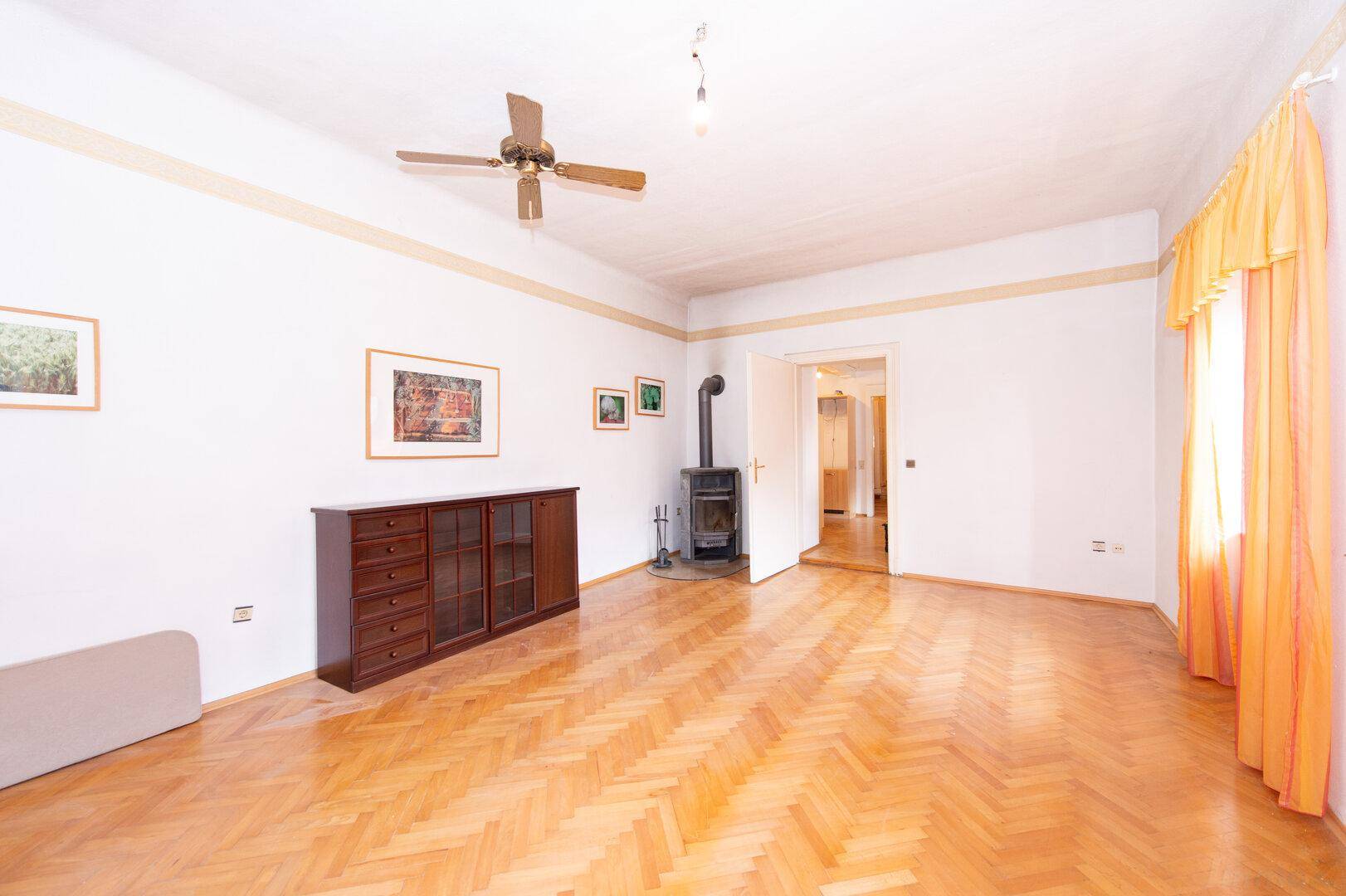 Großes Wohnzimmer mit Fischgrätparkett, Holzofen und Deckenventilator.