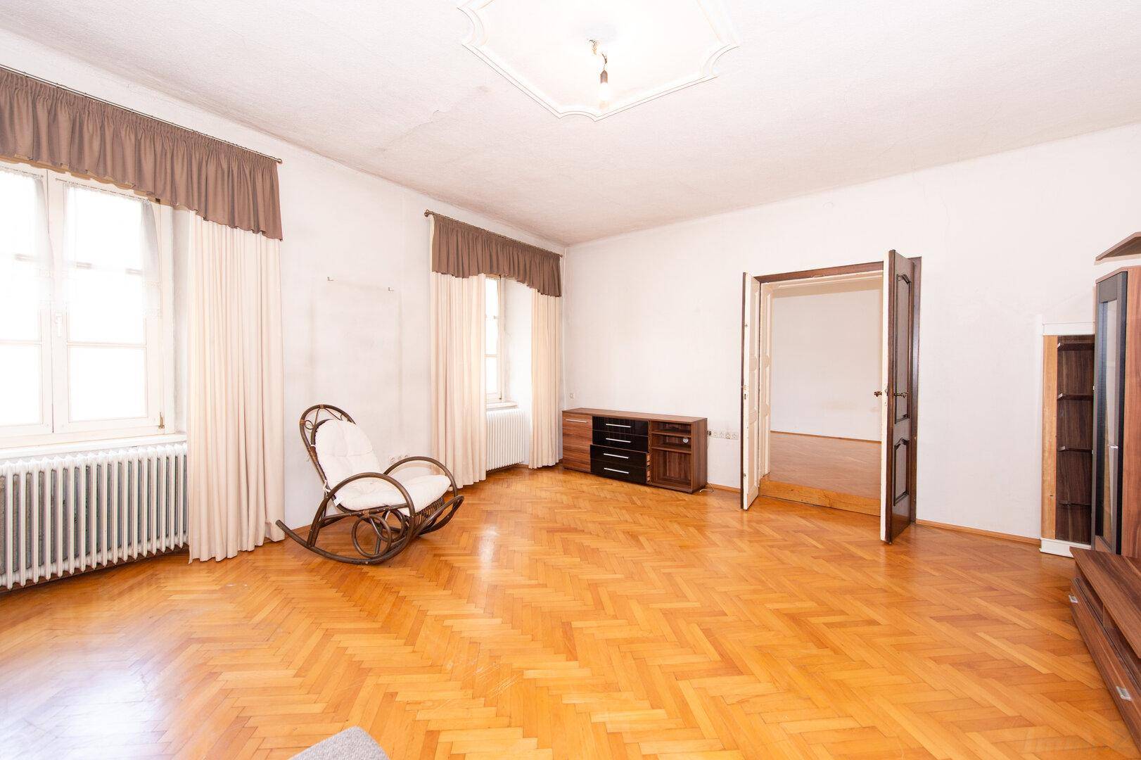 Helles Wohnzimmer mit Fischgrätparkett, großen Fenstern und einem Schaukelstuhl.
