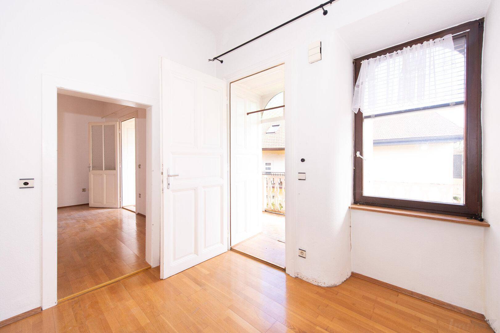 Helles Zimmer mit Parkettboden und Zugang zu einem Balkon.