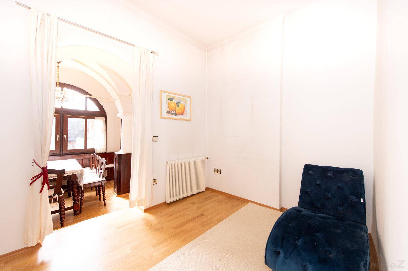 Heller Essbereich mit Holzboden, blauer Chaiselongue und Blick auf einen angrenzenden Raum.