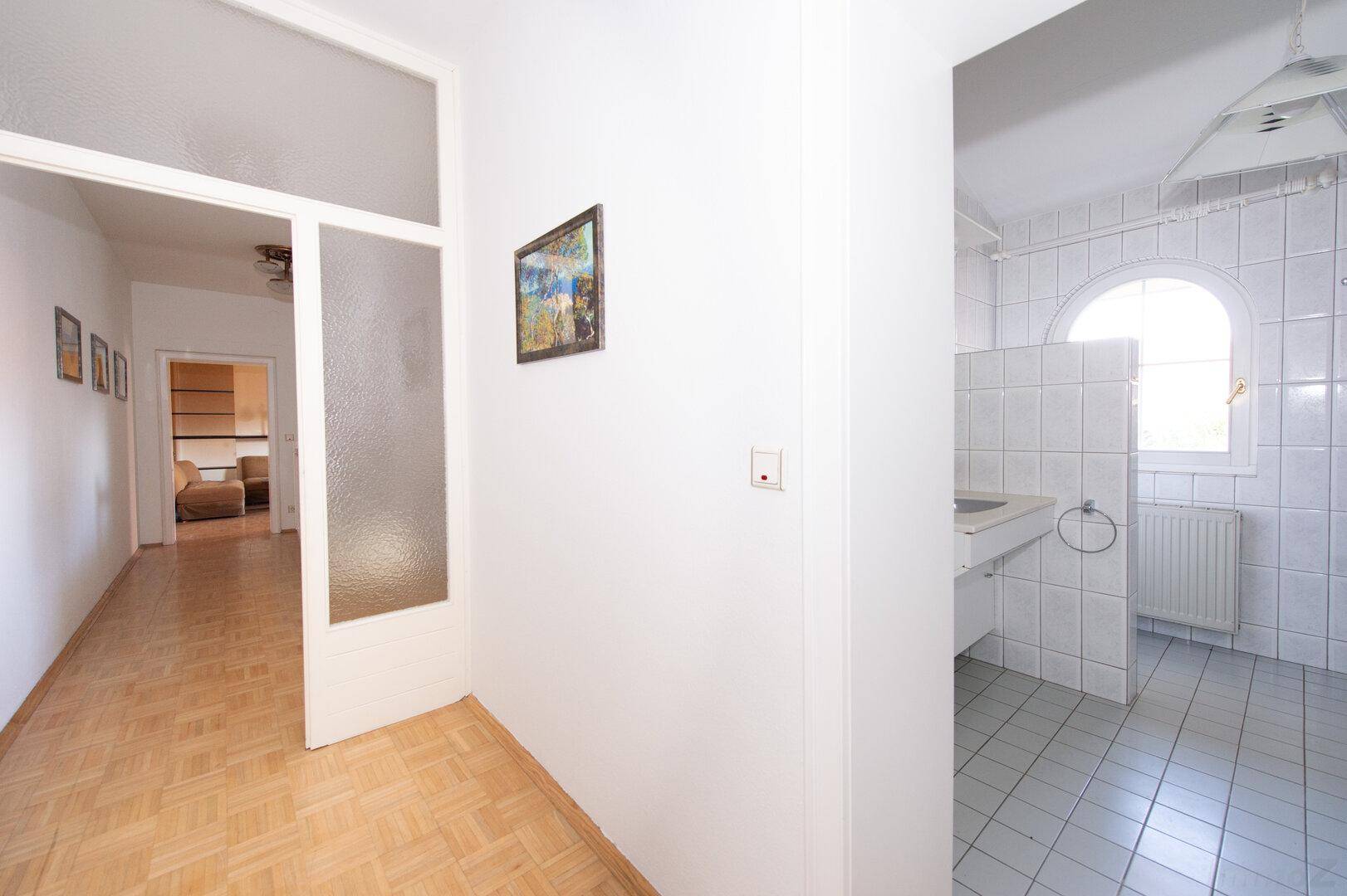Heller Flur mit Parkettboden und Zugang zu einem gefliesten Badezimmerbereich.