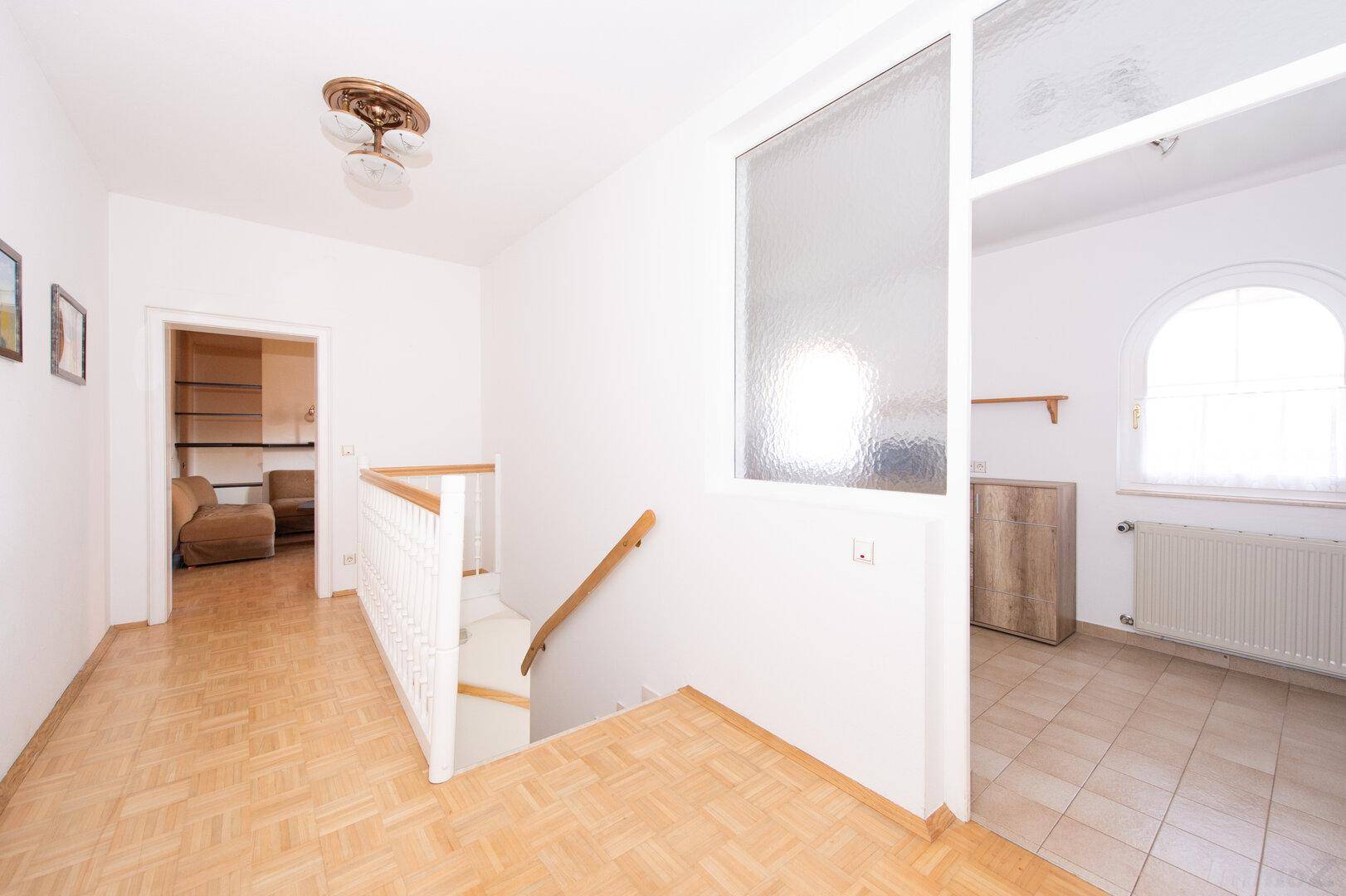Heller Flur mit Holzparkett und Treppe, die in ein unteres Stockwerk führt.