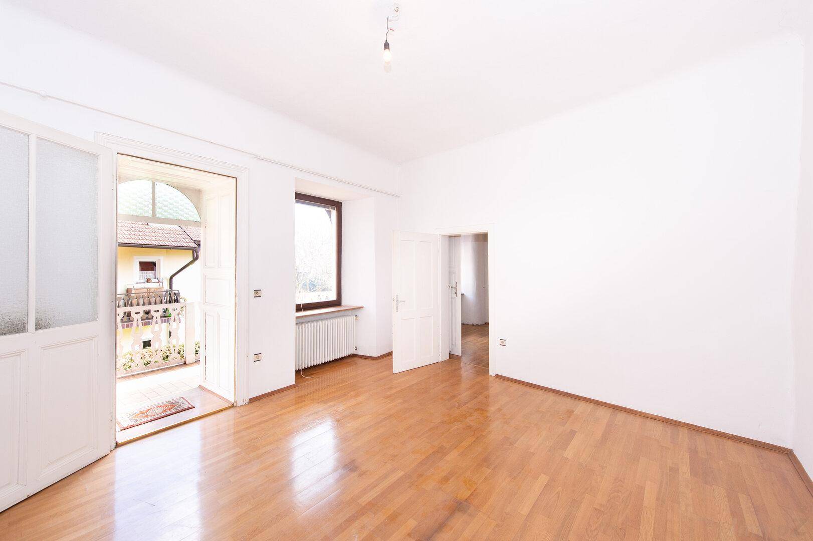 Helles Wohnzimmer mit Parkettboden und Zugang zu einem Balkon.