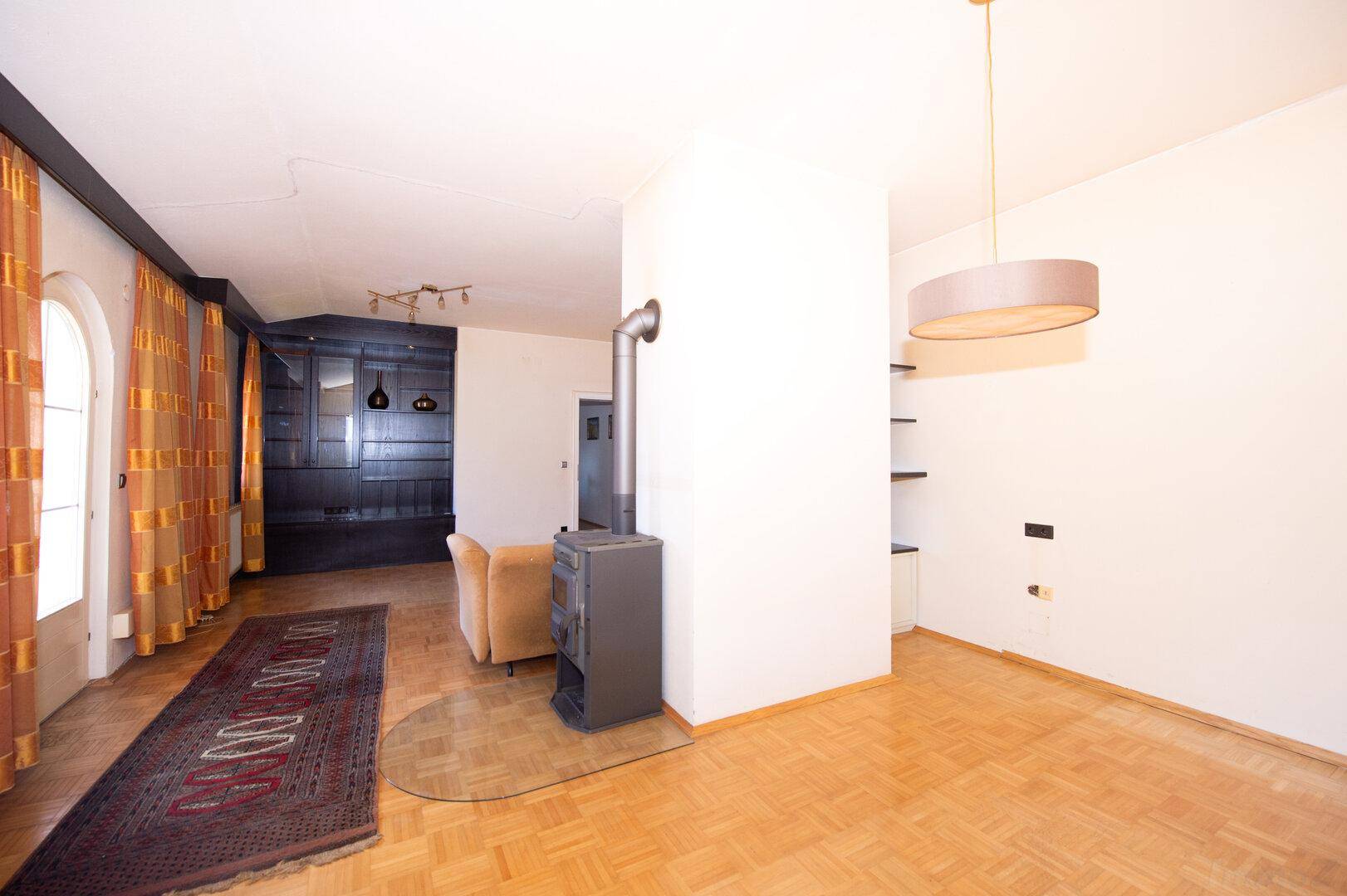 Helles Wohnzimmer mit Parkettboden, Kaminofen und Blick in einen weiteren Raum.