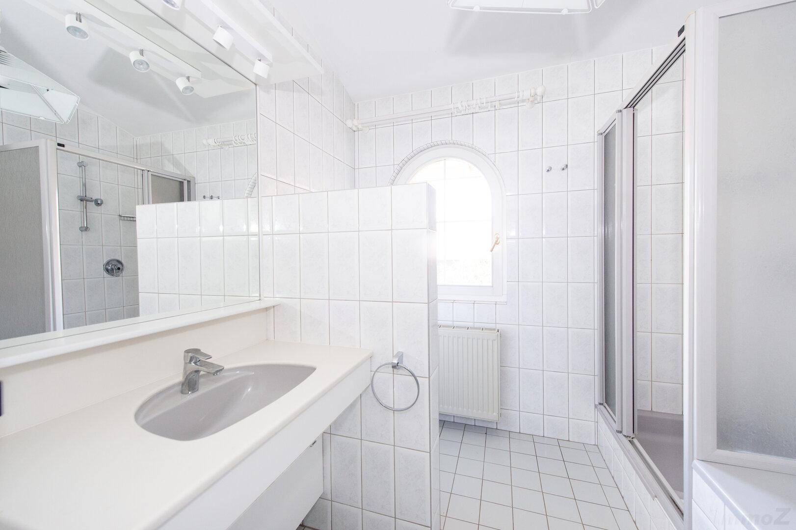Weiß gefliestes Badezimmer mit Waschbecken, Spiegel und Duschkabine.