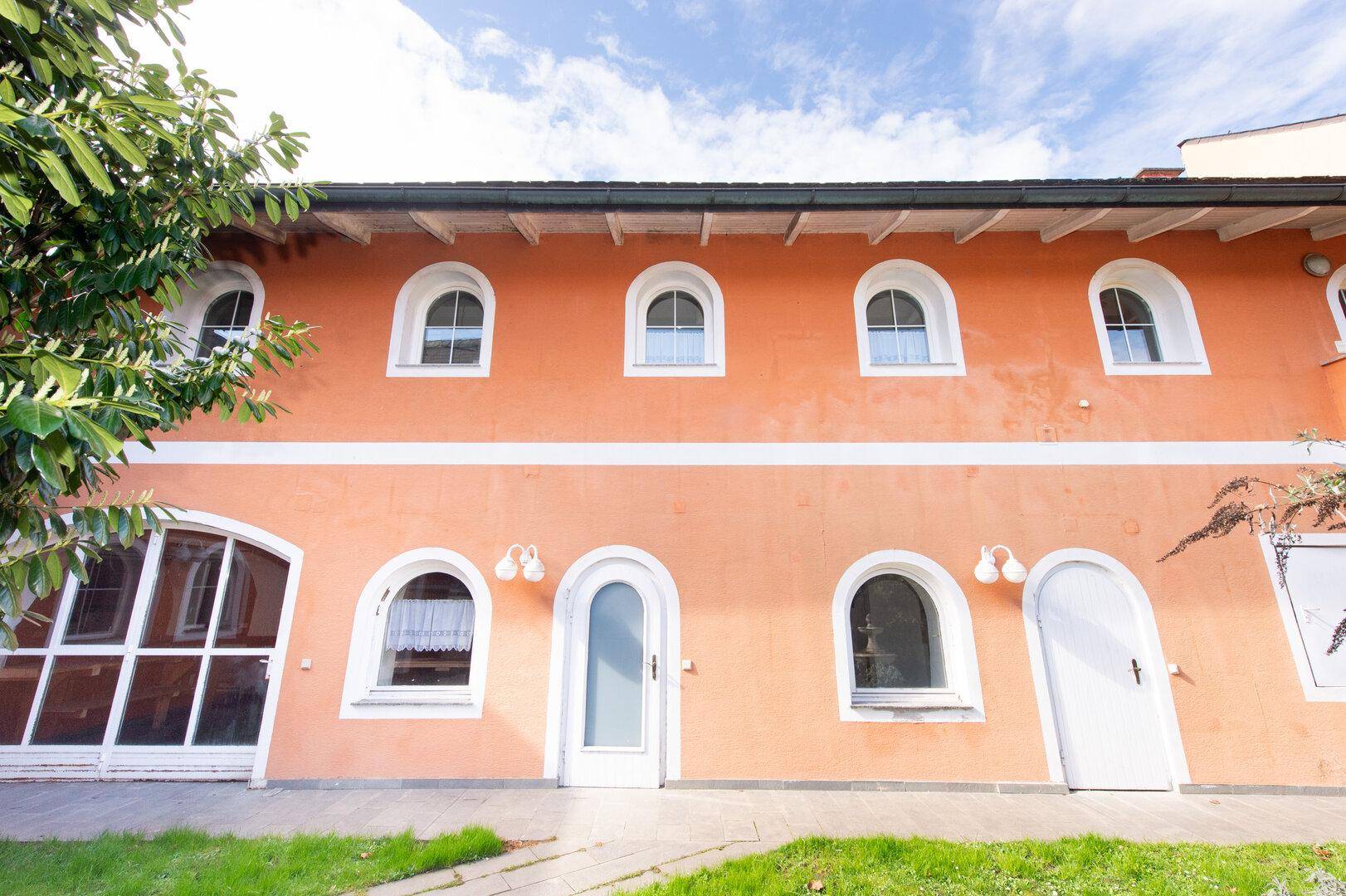 Orangefarbene Fassade eines Gebäudes mit vielen Rundbogenfenstern und einem grünen Rasen.