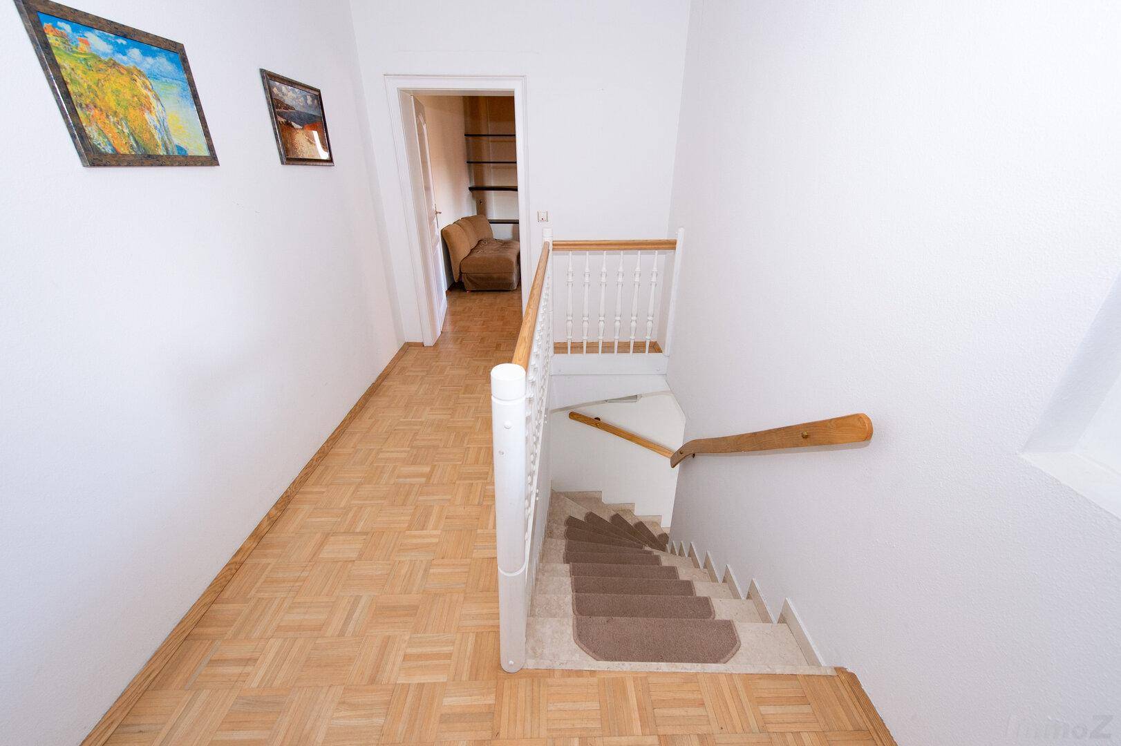 Heller Flur mit Holzparkett und Treppe, die zu einem oberen Stockwerk führt.