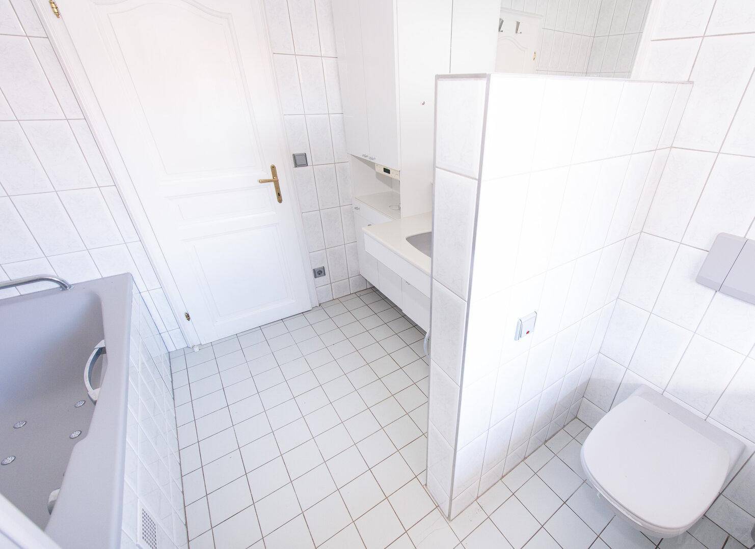 Weiß gefliestes Badezimmer mit Toilette, Badewanne und Tür.