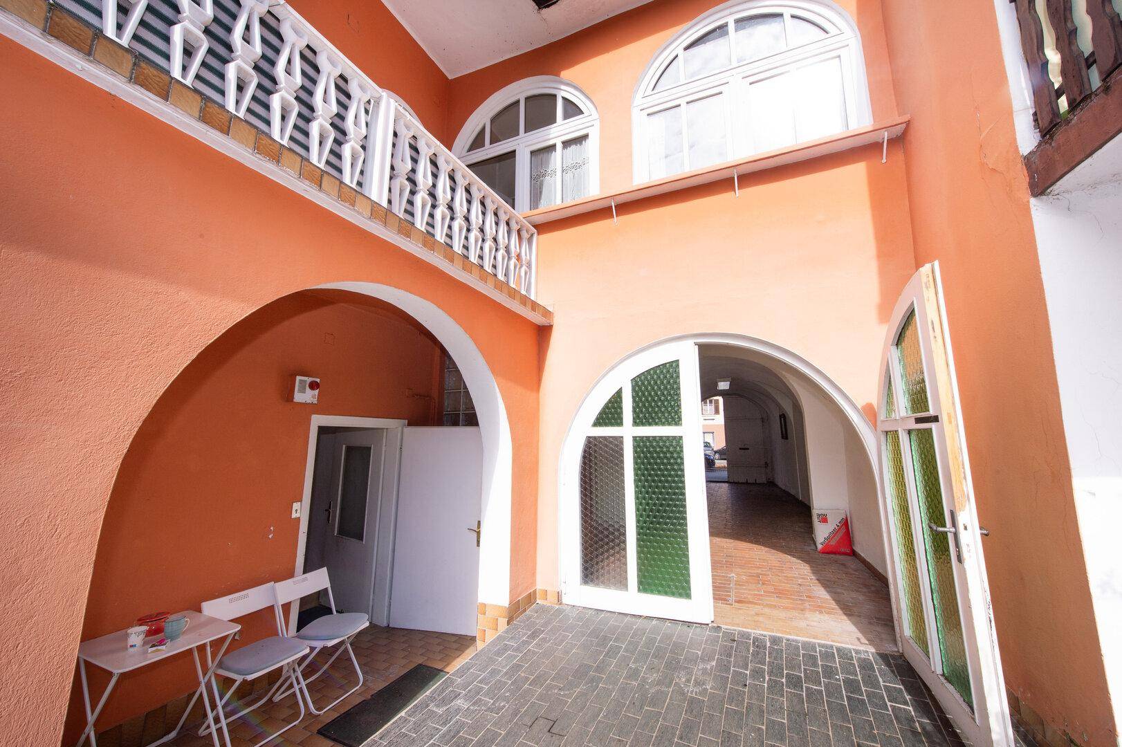 Überdachter Eingangsbereich mit Arkaden, Balkon und zwei Stühlen.