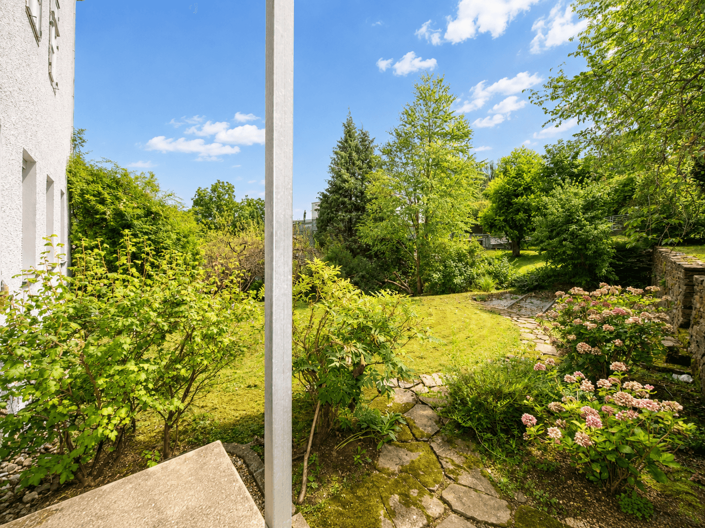 Sonniger Garten mit üppiger Vegetation, Steinpfaden und blühenden Sträuchern.
