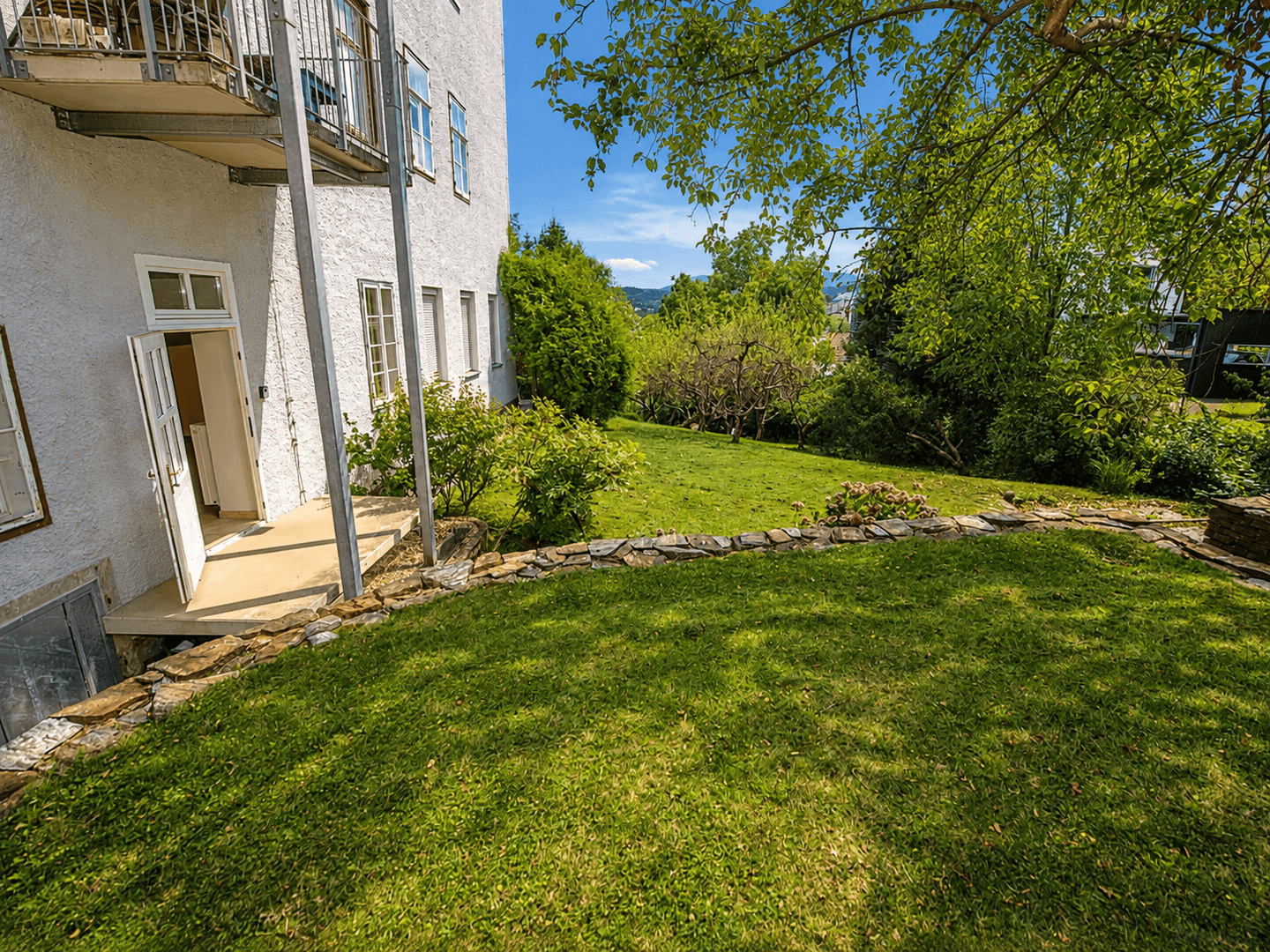Gepflegter grüner Gartenbereich mit Rasenfläche und Zugang zum Gebäude.