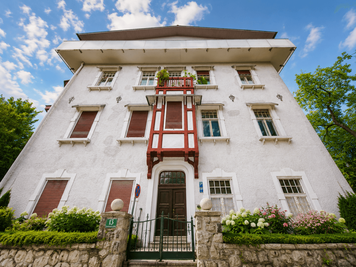 Historische Fassade des Gebäudes mit dekorativem Balkon und vielen Fenstern unter blauem Himmel.